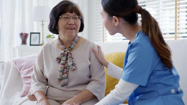 Older LGBTQ+ residents share conversation with a caregiver in a bright assisted living common room.