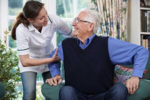 Older adult reviewing a care chart with a caregiver at a dining table with medications and a glass of water nearby.
