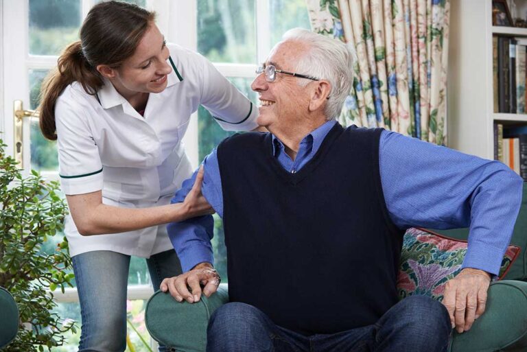 Older adult reviewing a care chart with a caregiver at a dining table with medications and a glass of water nearby.